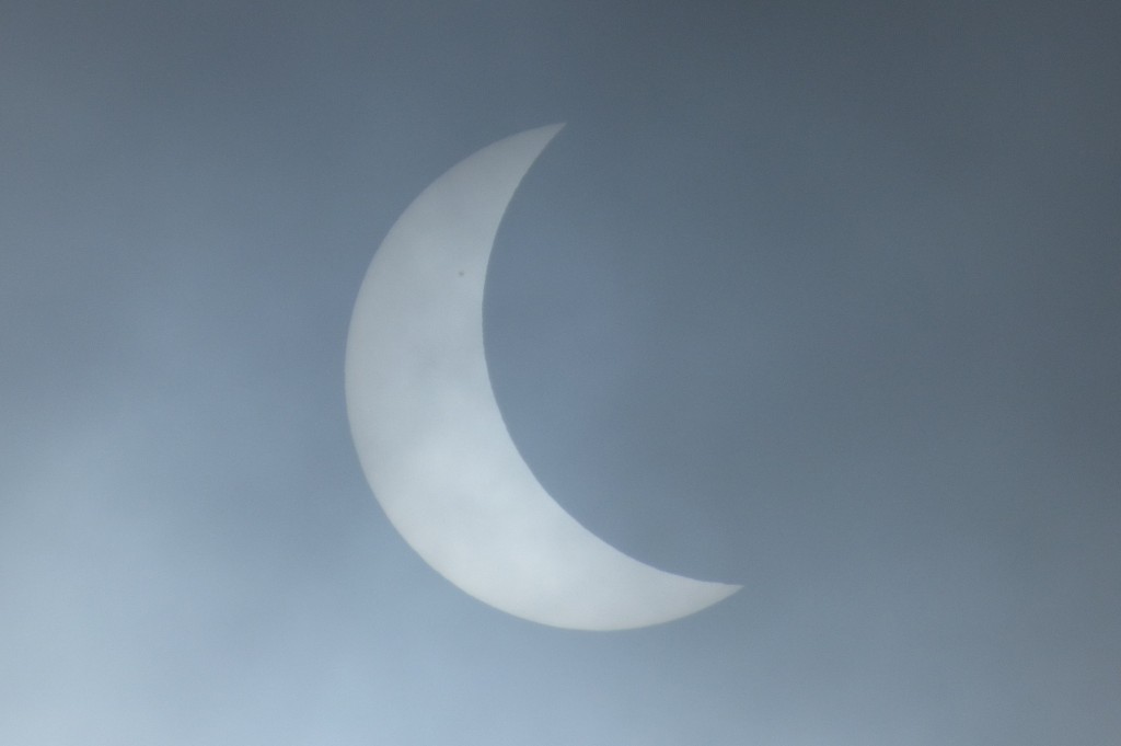 The moon starts to eclipse the sun, with a sunspot also visible on the solar surface.